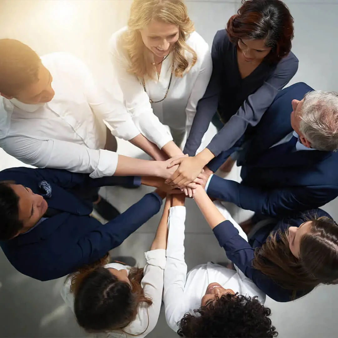 Un gruppo eterogeneo di persone si stringe la mano in un gesto di unità e lavoro di squadra, a simboleggiare l'impegno del Kaltan Group verso la collaborazione e l'emancipazione nel mondo degli affari.